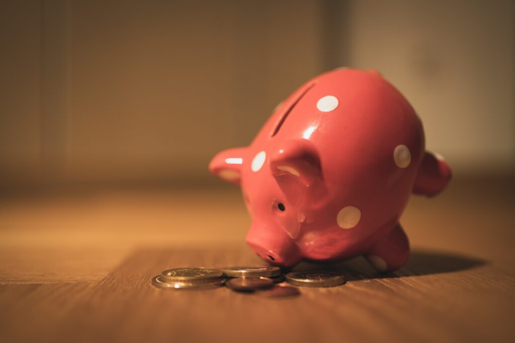 A pink piggy bank on a table surrounded by coins.